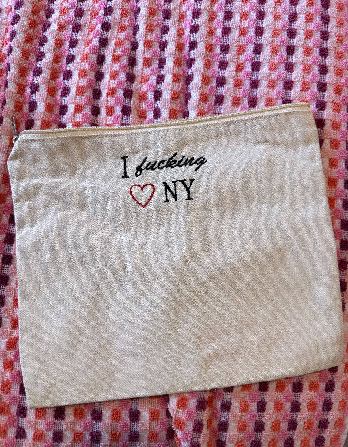 Beige pouch with 'I fucking love NY' text on a multicolored patterned fabric background